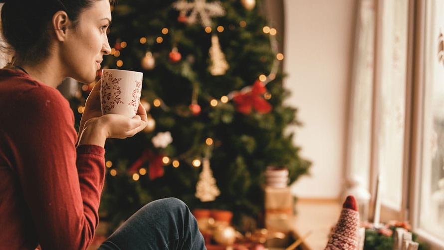 Young woman drinking tea by the Christmas tree.